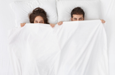 Junges Paar schaut unter Bettdecke hervor